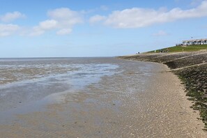 Ein Strand mit felsigem Ufer, einer grasbewachsenen Böschung und einem Gebäude im Hintergrund.