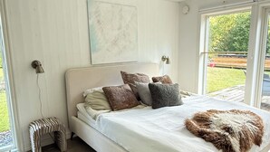 Un dormitorio con cama, almohadas, un taburete pequeño y un cuadro en la pared.