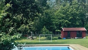 Una piscina con cubierta de madera y un edificio rojo al fondo.