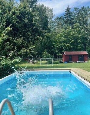 Une piscine avec une terrasse en bois et un b âtiment rouge en arrière-plan.