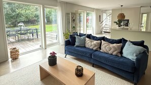 Un salón amplio con un sofá azul, una mesa de centro de madera y vistas a un patio con mobiliario exterior.