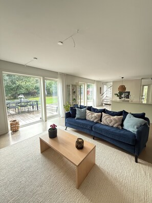 Un salón amplio con un sofá azul, una mesa de centro de madera y vistas a un patio con mobiliario exterior.