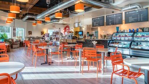 Ein modernes Café mit orangefarbenen Stühlen und Tischen, einer Pizza-Theke und einer Kaffeebereitungsstation.