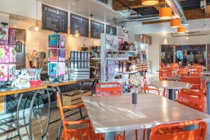 Ein Café-Interieur mit Tischen, Stühlen, einer Speisekarte und verschiedenen Gegenständen auf Regalen.