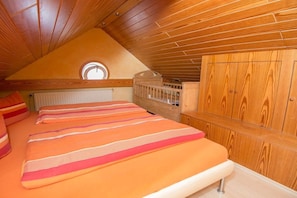 A bedroom with a sloped ceiling, wooden paneling, a bunk bed, a round skylight, and a wooden wardrobe. - Beach House Atlantic 32 (Norderney)