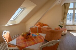 A cozy room with a sloped ceiling, a dining table with a fruit bowl, and orange furniture. - Beach House Atlantic 32 (Norderney)