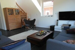 Ein Wohnzimmer mit einer Couch, einem Couchtisch mit einer Serviettenauslage, einem schwarzen Sessel, einem Holzschrank, einem Fernseher und einer Treppe.