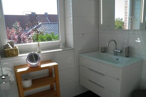 Ett badrum med ett fönster, ett handfat, en spegel och en hylla med en toalettpappersrulle.