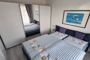 A bedroom with a bed, a wardrobe, a bedside table, and a framed picture on the wall. - Nautilus Penthouse Beach View (Cuxhaven)