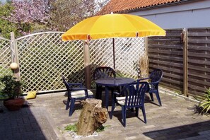 An outdoor patio with a table and chairs, a yellow umbrella, and a wooden fence. - Holiday apartment in Borkum with barbecue (Borkum)