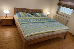 A bedroom with a wooden bed, two bedside lamps, a window with blinds, and a radiator. - Holiday apartment in Borkum with barbecue (Borkum)