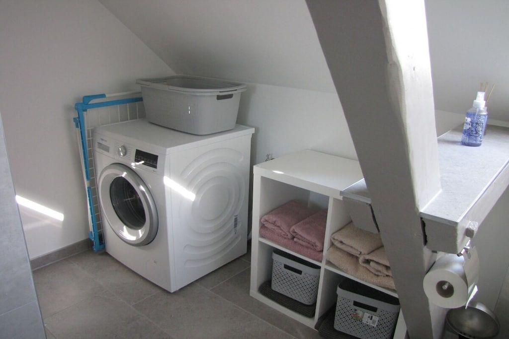 A laundry area with a washing machine, a drying rack, and storage shelves with folded towels.
