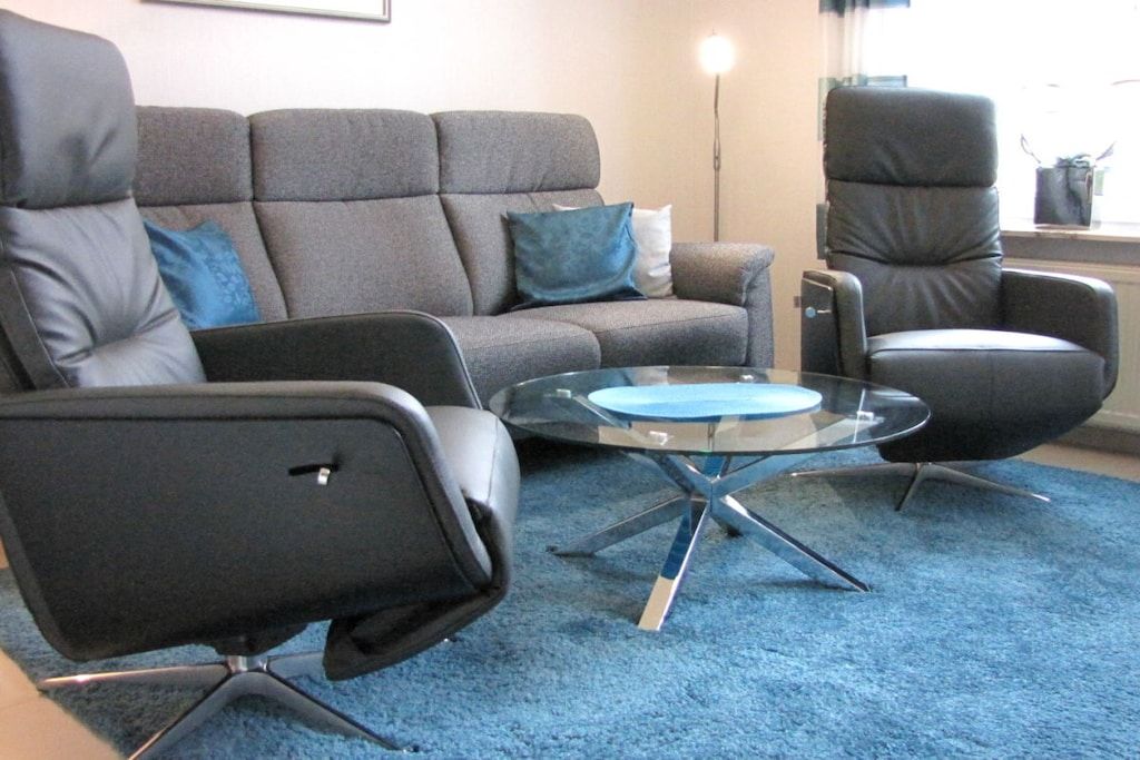 A living room with a grey sofa, a black armchair, and a glass coffee table.