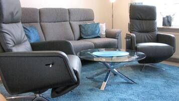 A living room with a grey sofa, a black armchair, and a glass coffee table.