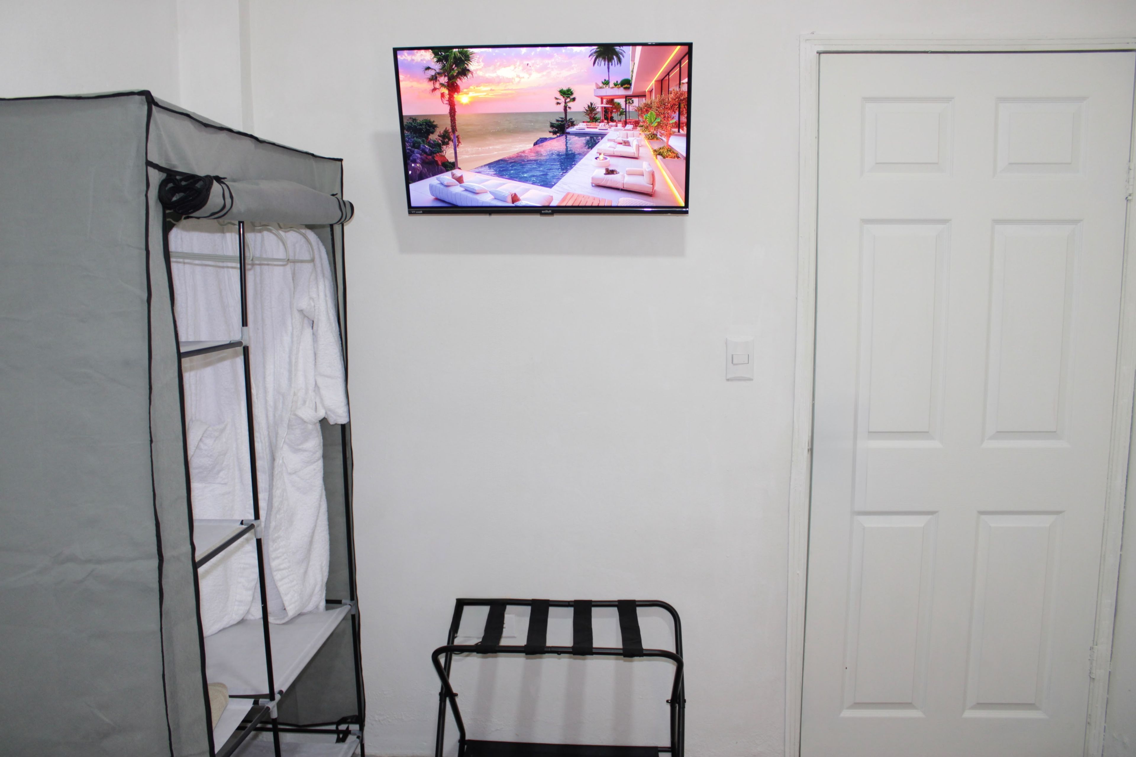 A room with a bed, a TV mounted on the wall displaying a sunset view, a white door, and a towel rack.