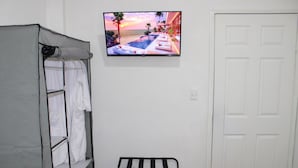 Huoneessa on sänky, seinälle asennettu televisio, josta näkyy auringonlasku, valkoinen ovi ja pyyheteline.