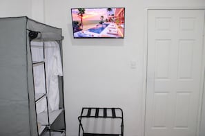 Quarto com cama, televisão fixada na parede exibindo vista do pôr do sol, porta branca e porta-toalhas.