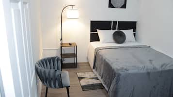 Une chambre à coucher comprenant un lit, une chaise, une table de chevet, une lampe et une œuvre d’art murale.