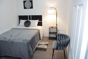 Quarto com cama, cadeira, mesa de cabeceira e abajur.