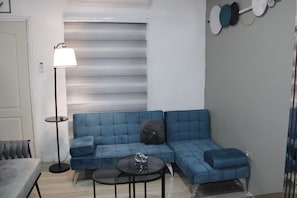 Uma sala de estar moderna com um sofá em formato de L azul, uma mesinha de centro redonda e um abajur.