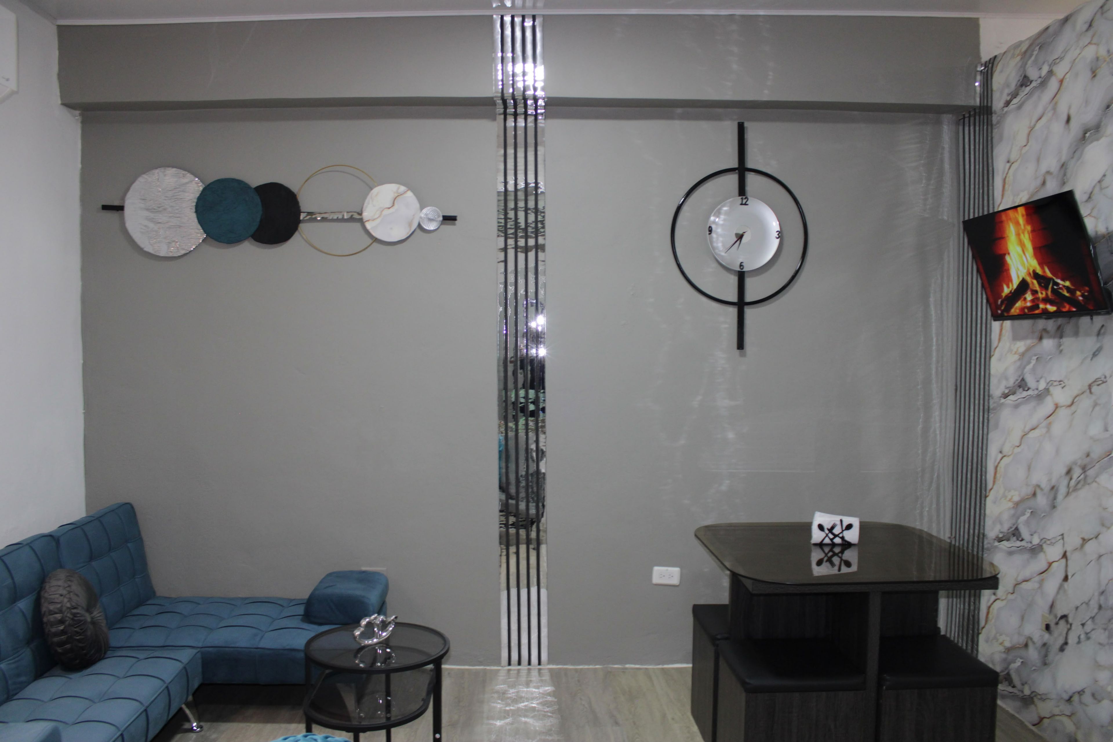 Un salon moderne avec un canapé d’angle, une petite table ronde et un téléviseur fixé sur un mur en marbre.
