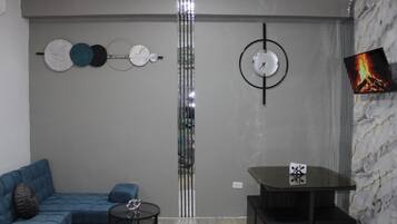 A modern living room with a sectional sofa, a small round table, and a TV mounted on a marble wall.