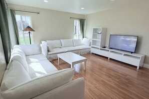 Een woonkamer met een witte bank, een salontafel, een tv op een meubel en een lamp.