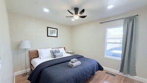 Ein Schlafzimmer mit einem Bett, einem Deckenventilator, einem Fenster mit Vorhängen und einem Bild an der Wand.