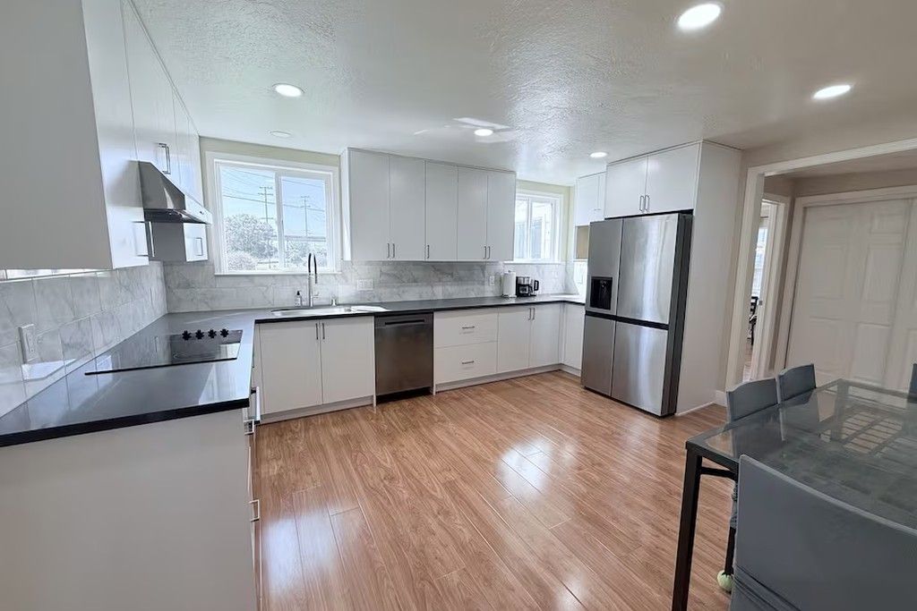 A modern kitchen with white cabinets, stainless steel appliances, and a glass dining table.