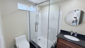 Ein Badezimmer mit einer Duschkabine aus Glas, einer weißen Toilette und einem Waschtisch mit schwarzer Arbeitsplatte.