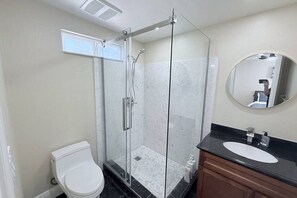 Casa de banho com cabine de duche em vidro, sanita branca e espelho com bancada preta.