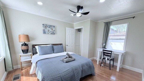 Ein Schlafzimmer mit einem Bett, einem Schreibtisch, einem Stuhl, einem Deckenventilator und einem Fenster.