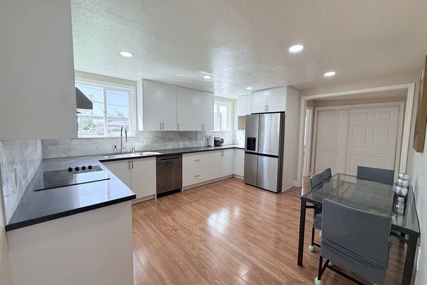 A modern kitchen with white cabinets, a stainless steel refrigerator, and a glass dining table.