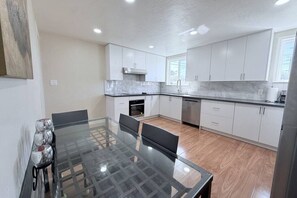 Uma cozinha moderna com armários brancos, uma mesa de jantar de vidro e um exaustor de aço inoxidável.