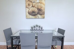 Een eetruimte met een tafel met glazen blad, vier grijze stoelen en een kandelaar met kaarsen.