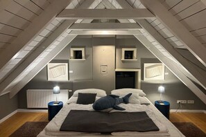 Ein Schlafzimmer mit schrägem Dach, einem Bett mit blauem Kissen, Nachttischlampen und einer Heizung.