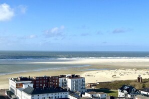 Eine Küstenstadt mit Gebäuden in Strandnähe, einem klaren Himmel und dem Meer im Hintergrund.
