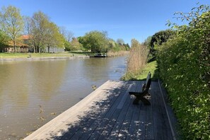 A calm river with a wooden dock and a bench, surrounded by greenery and trees. - Holiday apartment with 1 bedroom (Krummhörn-Greetsiel)