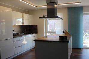 Una cuina moderna amb armaris blancs, una illa central i una finestra que deixa entrar llum natural.