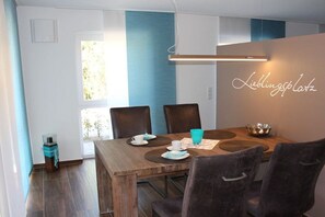 A dining area with a wooden table, four chairs, and a neon sign on the wall. - Holiday apartment with 1 bedroom (Krummhörn-Greetsiel)
