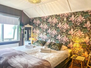 Ein Schlafzimmer mit einem großen Bett, einem Spiegel, einem Fenster und tropischem Wandpapier.