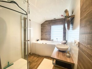 Ein modernes Badezimmer mit einer Duschkabine aus Glas, einer freistehenden Badewanne und einem Holzbadezimmer-Möbel mit einem Aufsatzbecken.