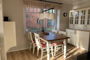 A kitchen with a dining table, chairs, a window with a view of a brick building, and white cabinets. - Holiday apartment with 2 bedrooms (Wangerooge)