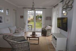 A living room with a sofa, two wicker chairs, a coffee table, a TV, and a large window with a view of the outdoors. - Holiday apartment with 2 bedrooms (Wangerooge)