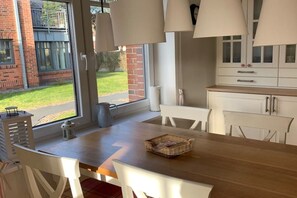 Een eetruimte met een houten tafel, witte stoelen en uitzicht op een bakstenen gebouw.