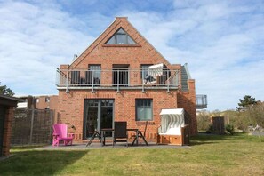 Een tweelaags bakstenen huis met een balkon, een schuifdeur en een zithoek buiten.