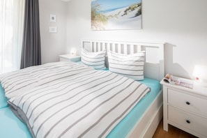 Ein ordentlich gemachtes Bett mit gestreifter Bettwäsche, ein weißer Kopfteil und ein Nachttisch mit einer Lampe und einer Zeitschrift.