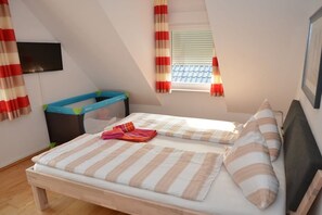 A bedroom with a bed, a window with curtains, a television on the wall, and a small play area. - MeerZeit - Süderpfad 2b (Borkum)