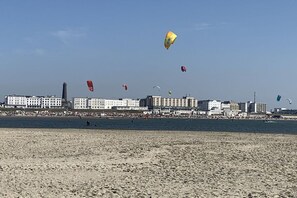 A beach with buildings in the background and kites flying in the sky. - MeerZeit - Süderpfad 2b (Borkum)