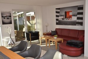 Een moderne woonkamer met een rode bank, een zwarte fauteuil, een houten salontafel en een glazen deur die uitkomt op een balkon.